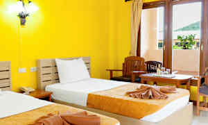 Ett hotellrum med gula väggar, två sängar med gulorange överkast, och ett fönster med utsikt. (AI-genererad text)