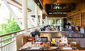 Restaurang med dukade bord och fönster med utsikt över grönska. (AI-genererad text)