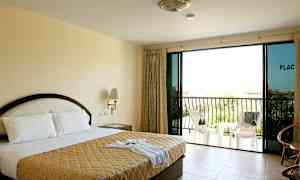 Ett hotellrum med en dubbelsäng, sängbord, glasdörrar och en balkong med stolar. (AI-genererad text)