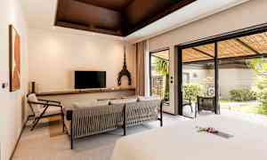 Ett hotellrum med modern inredning, en sittgrupp, en TV, och stora glasdörrar som leder till en grönskande terrass. (AI-genererad text)