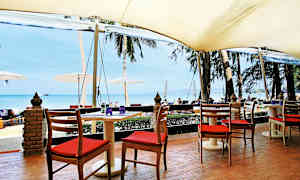 Sittplatser vid ett bord under ett markistak med utsikt över stranden och havet. (AI-genererad text)