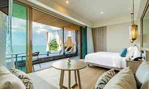 Rum med havsutsikt, säng, bord samt soffa och uteplats med solstolar. (AI-genererad text)