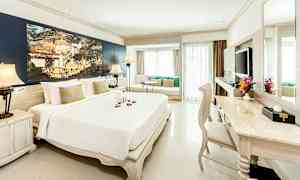 Ett ljust och elegant hotellrum med en stor säng, sittgrupp vid fönstret och ett skrivbord med stol. (AI-genererad text)