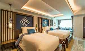 Ett hotellrum med två breda sängar, dekorerade med vita lakan och blå kuddar, samt ett stort fönster med gardiner. (AI-genererad text)