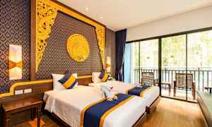 Ett hotellrum med två enkelsängar, dekorerade med blå och gula sängkläder och kuddar. Väggen bakom sängarna är dekorerad med ett extravaganta gyllene mönster och motiv. Ett stort fönster längst bort visar en balkong med stolar och utsikt över grönska. (AI-genererad text)