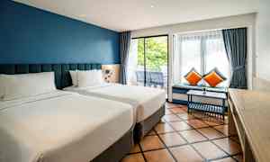 Två enkelsängar i ett hotellrum med blå väggar och stora fönster. (AI-genererad text)