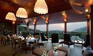 En modern restaurang eller lounge med elegant inredning, stora fönster och utsikt över en skog och kullar i bakgrunden. (AI-genererad text)