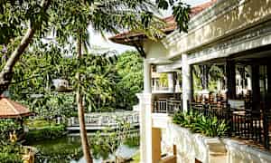 En terrass i en tropisk trädgårdsomgivning med frodig grönska och en liten damm. (AI-genererad text)