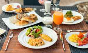 En frukostservering med olika rätter som omelett, sallad, bakverk, juice och frukt, upplagt på tallrikar vid ett bord. (AI-genererad text)