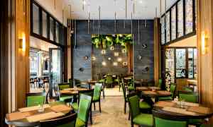 Restaurang med bord och stolar, gröna inslag och dekorativa väggdetaljer. (AI-genererad text)