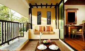 En uteplats med en soffa dekorerad med kuddar, ett litet bord med frukt och tallrikar samt utsikt mot grönska. (AI-genererad text)