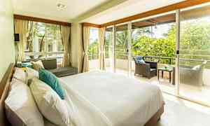 Ett ljust och rymligt sovrum med stor säng, soffgrupp och en balkong med utsikt över grönska. (AI-genererad text)