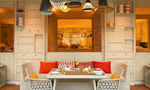 Ett bord med dukning står framför en soffa och två stolar på en uteplats med dekorativa lampor. (AI-genererad text)