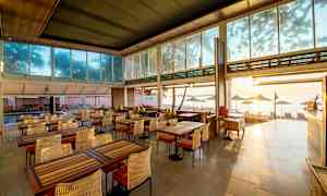 En restaurang med utsikt över stranden, möblerad med bord och stolar. (AI-genererad text)