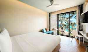 Modernt hotellrum med utsikt över hav och palmer genom ett fönster. (AI-genererad text)