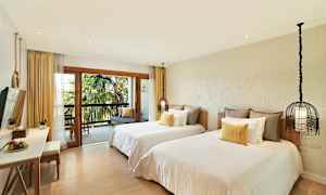 Hotellrum med två separata bäddar, en balkong med utsikt över palmer, och en sittgrupp. (AI-genererad text)