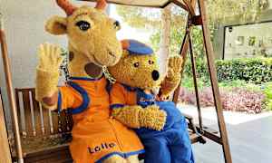 Två karaktärer i gosedjursdräkter, en giraff och en björn, sitter på en gungstol och vinkar. (AI-genererad text)