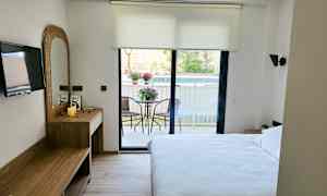 Ett hotellrum med en dubbelsäng, skrivbord, TV och en balkong med trädgårdsmöbler. (AI-genererad text)