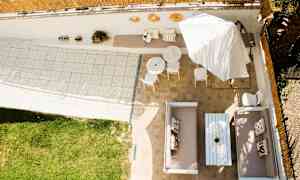 Vy över en uteplats med sittgrupper, bord, parasoll och gräsyta. (AI-genererad text)