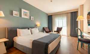 Ett hotellrum med en dubbelsäng, två fåtöljer vid ett bord, ett skrivbord och en TV. (AI-genererad text)