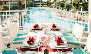 Ett bord uppdukat med röda servetter och vita tallrikar vid en swimmingpool. (AI-genererad text)