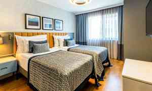 Ett hotellrum med två enkelsängar, modern inredning och naturligt ljus från ett fönster. (AI-genererad text)