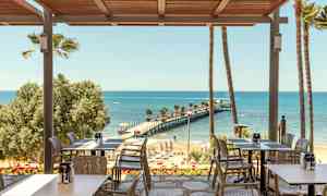 En restaurang med utsikt över en strand och en brygga som sträcker sig ut i havet. (AI-genererad text)