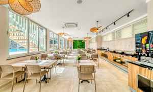 Ett modernt och ljust matområde med många bord och sittplatser, stora fönster mot en pool och en växtvägg längst bort. (AI-genererad text)