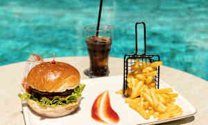 En hamburgare, pommes frites och en glas läsk på ett bord vid en pool. (AI-genererad text)