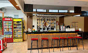 En bar med höga röda stolar och en upplyst bardisk. Bakom finns drycker och shishor. (AI-genererad text)