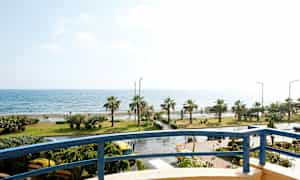 Utsikt från en balkong mot en kustlinje med palmer och hav. (AI-genererad text)