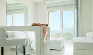 Ett ljust, modernt rum med vita möbler, stora fönster med utsikt över havet och dekorativa detaljer på en bordsyta. (AI-genererad text)