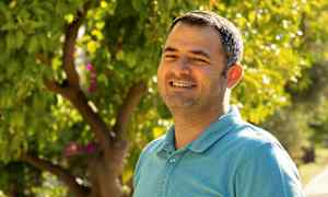 En person i en blå skjorta står framför en grönskande trädgård. (AI-genererad text)