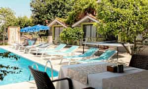 En utomhuspool bredvid solstolar, bord och stolar belägna nära små byggnader. (AI-genererad text)