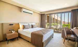 Ett hotellrum med en stor säng, nattduksbord och en balkong med utsikt. (AI-genererad text)