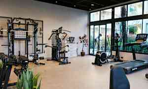 Ett gym med olika träningsmaskiner och vikter, samt glasfönster som visar utsikten utanför. (AI-genererad text)