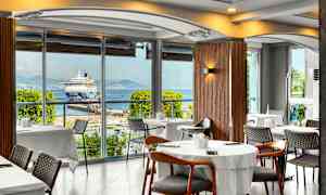 Restaurang med utsikt mot en kryssningsfartyg vid en hamn. (AI-genererad text)