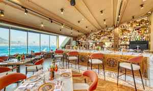 Restaurang med utsikt över havet, bord och stolar, samt en välfylld bar. (AI-genererad text)