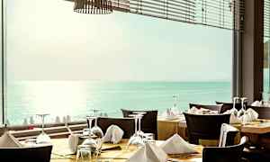 Restaurang med dukade bord framför ett fönster med utsikt över havet. (AI-genererad text)