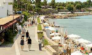 En gångväg vid havet med människor som promenerar och personer som kopplar av på solstolar under parasoller. (AI-genererad text)