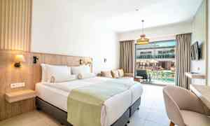 Hotellrum med dubbelsäng, soffa och utsikt mot en pool. (AI-genererad text)