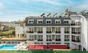 Ett hotell med vit fasad och flera fönster och balkonger, en pool framför byggnaden. (AI-genererad text)