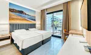 Hotellrum med två enkelsängar, balkong i bakgrunden och stort fotografi av en strand på väggen. (AI-genererad text)