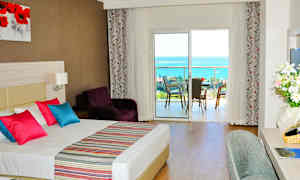 Hotellrum med dubbelsäng, färgglada kuddar och utsikt över en balkong med havsutsikt. (AI-genererad text)