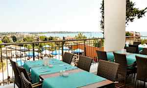 Utsikt från en restaurang med dukade bord och stolar, utomhusområde med parasoller och havet i bakgrunden. (AI-genererad text)