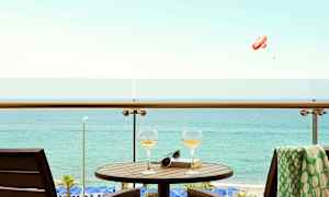 En balkong med bord, två glas och en bok med utsikt över havet. (AI-genererad text)