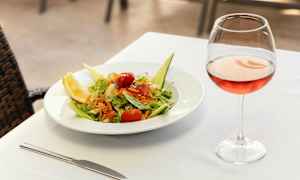En tallrik med sallad och ett glas rosévin på ett dukat bord. (AI-genererad text)