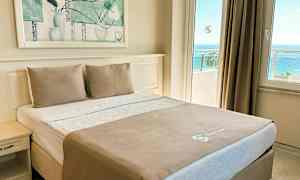 Ett hotellrum med en dubbelsäng med vita och beige sängkläder, ett nattduksbord och ett panoramafönster med havsutsikt. (AI-genererad text)