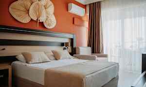 Hotellrum med orange vägg, dubbelsäng med två kuddar och dekorativa föremål ovanför sängen. (AI-genererad text)