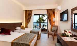 Hotellrum med två enkelsängar, fönster med utsikt mot palmer och hav. (AI-genererad text)